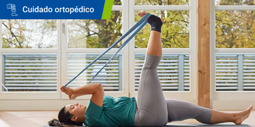 Una mujer con tobillera se tumba en el suelo y utiliza una banda elástica para estirar la pierna. Una mujer con tobillera se tumba en el suelo y utiliza una banda elástica para estirar la pierna.